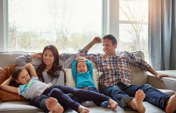 Ludzie, którzy naprawdę się liczą. szczęśliwa młoda rodzina czworga relaksujących się razem na kanapie w domu - Zdjęcie, obraz