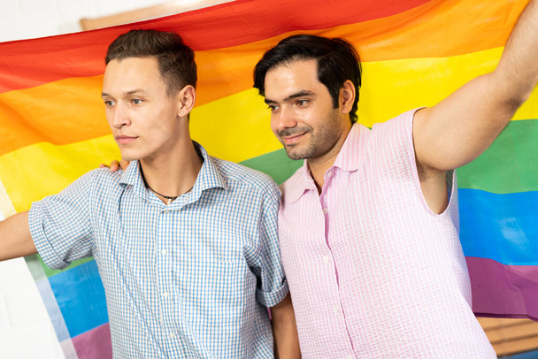 Schwules Paar mit lgbt Regenbogenfahne zu Hause. Selektiver Fokus. Schwules Paar umarmt und zeigt seine Liebe mit Regenbogenfahne. LGBT und Liebe. Gay Pride und Regenbogenhintergrund. - Foto, Bild