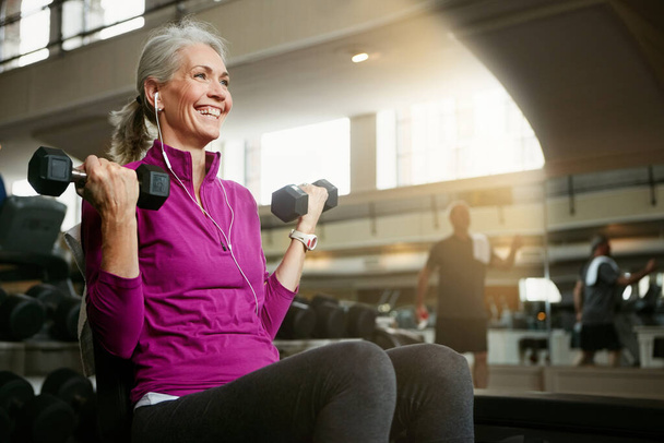 Vive, ríe, ama, levanta. Retrato de una mujer mayor feliz haciendo ejercicio con pesas en el gimnasio - Foto, Imagen