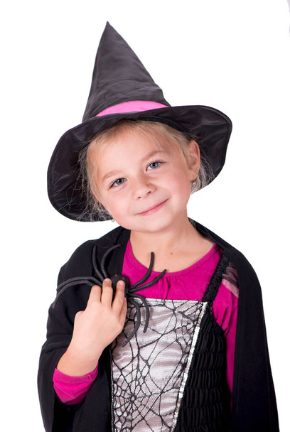 Egy gyönyörű lány boszorkányjelmezben, kalapban, egy pókkal a kezében, világos háttérben, másolja a helyet. A boszorkány meglengeti a varázspálcáját. Boldog Halloweent!. - Fotó, kép