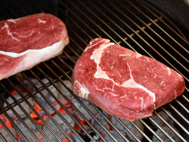 Raw Rib Eye Steak on grill grate over charcoal grill, preparing beef steaks on barbecue. - Photo, Image