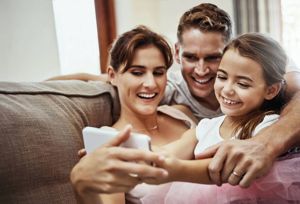Right, now hold it still and then press the button...a little girl taking a selfie with her parents at home - Photo, image