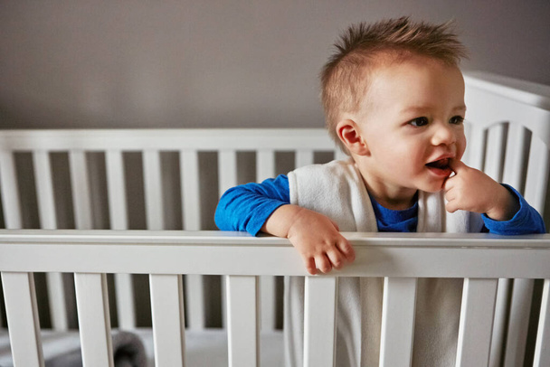 its their world, we just live in it. a cute little baby boy standing in his cot - Photo, Image