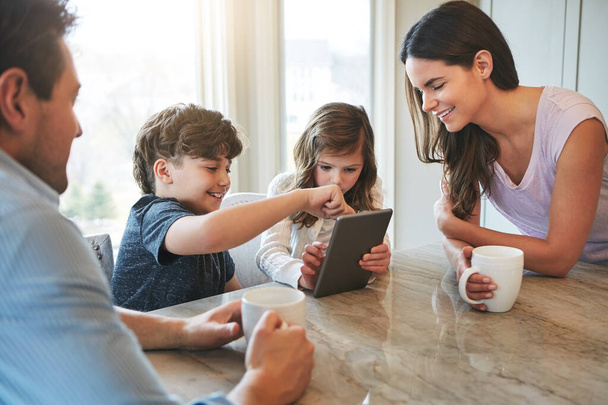 Surfs up, kids. a married couple and their young children playing with a tablet together in their kitchen - Foto, Imagen