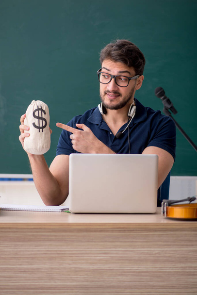 Young music teacher holding moneybag in the classroom - Photo, Image