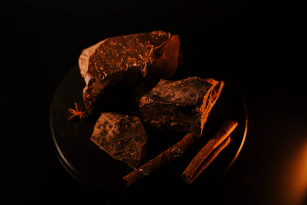 Chocolade. Stukjes pure chocolade draaien op donkere achtergrond, draaien. Gourmet dessert ingrediënt. Suikerwerk, begrip suikerwerk. - Foto, afbeelding