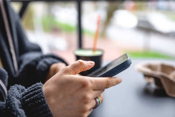 Una mujer se sienta en la terraza de un café y utiliza un teléfono inteligente, de cerca con un gadget. - Foto, Imagen