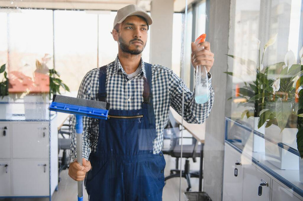 Male janitor cleaning window in office. - Фото, зображення