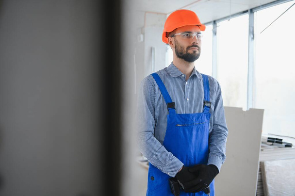 Portrait of young and hardworking constructor posing in big unfinished room. Building concept. - Foto, Bild
