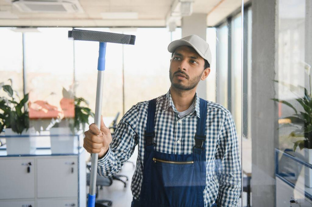 Male janitor cleaning window in office. - Fotoğraf, Görsel