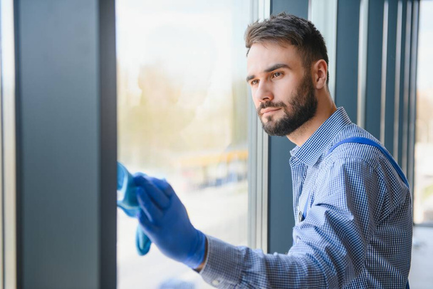 Male janitor cleaning window in office. - Valokuva, kuva