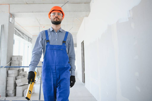Portrait of young and hardworking constructor posing in big unfinished room. Building concept. - 写真・画像