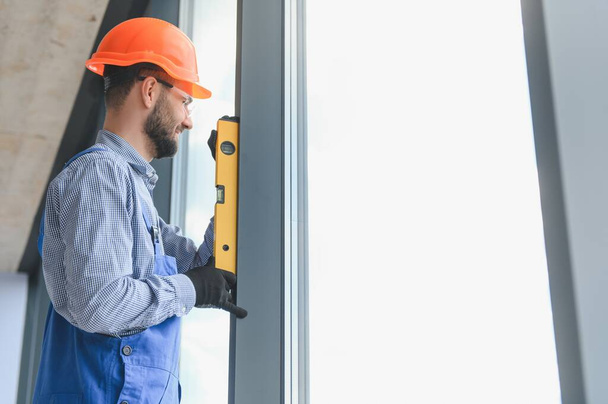 Workman in overalls installing or adjusting plastic windows in the living room at home. - Fotografie, Obrázek