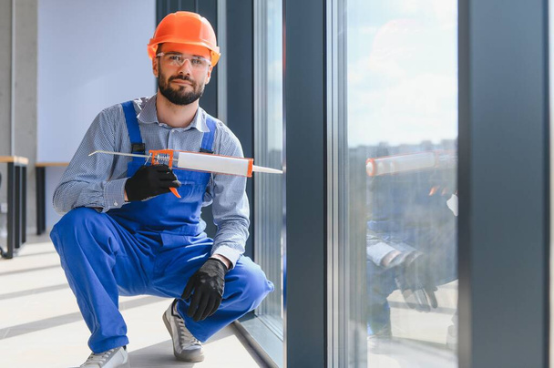 Workman in overalls installing or adjusting plastic windows in the living room at home. - Фото, изображение