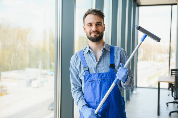 Young man cleaning window in office. - Foto, Bild