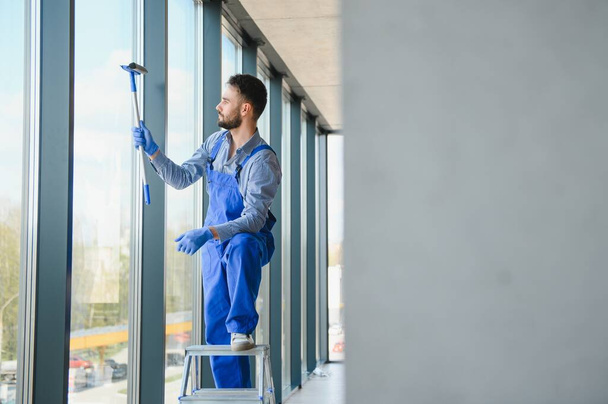 Male janitor cleaning window in office. - Foto, afbeelding