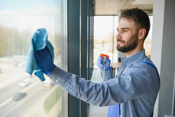 Young man cleaning window in office. - Foto, imagen
