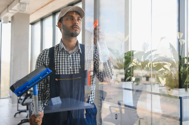 Young indian man washing window in office - Foto, Imagem