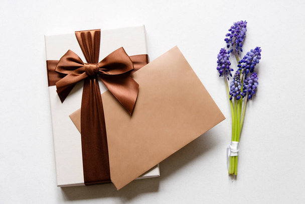 Flat lay composition with muscari flowers, gift box and envelope mockup with blank greeting card on light background. Minimal floral frame. Happy mother's day, women's day, birthday or wedding. - Photo, image