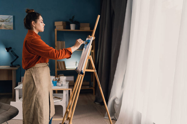 νεαρή Βραζιλιάνα καλλιτέχνης γυναίκα στο σπίτι στούντιο στέκεται κοντά στον καμβά αρχίζει να ζωγραφίζει μια νέα εικόνα. Μαύρα μαλλιά, ντυμένα με καθημερινά ρούχα. έννοια της δημιουργικότητας και χόμπι. Μπάνερ. αντίγραφο χώρου. - Φωτογραφία, εικόνα