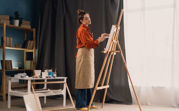 Resim stüdyosunda sehpası olan güzel bir kadın ressam. Genç ve yetenekli bir sanatçı çalışıyor. Boşluğu kopyala - Fotoğraf, Görsel