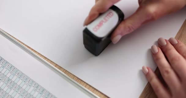 Рука жінки ставить штамп Завершений на порожній чистий аркуш паперу в офісі. Клерк розміщує позначку на офіційному документі на робочому місці повільний рух
 - Кадри, відео