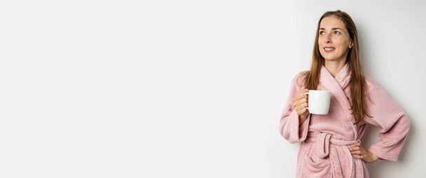 Usmívající se mladá žena v županu s šálkem na bílém pozadí. Nápis. - Fotografie, Obrázek