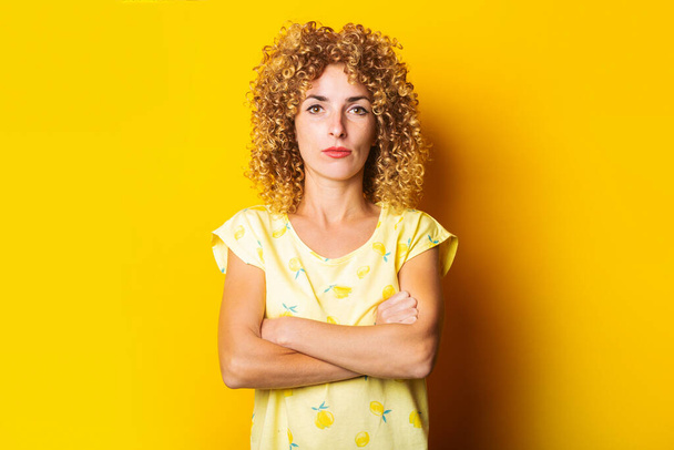 serious beautiful curly young girl with crossed arms on a yellow background. - Foto, Bild