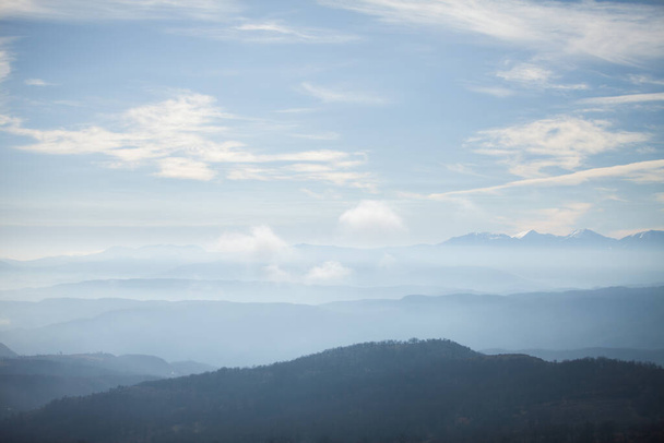 συννεφιασμένος ουρανός και επικαλυπτόμενα στρώματα των περιγραμμάτων των βουνών, εναέρια προοπτική και περίγραμμα των βουνών με ομίχλη και σύννεφα - Φωτογραφία, εικόνα