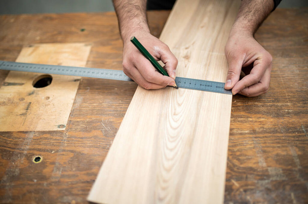Carpenter measuring a wooden plank on the work bench - Foto, Imagen