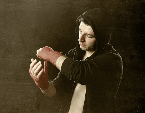 Man in boxing hoodie jumper with hood on head wrapping hands wrists before gym training - Photo, Image