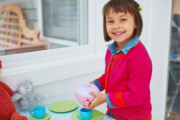 ¿Quieres una taza de té? Retrato de una adorable niña haciendo una fiesta de té en casa - Foto, imagen