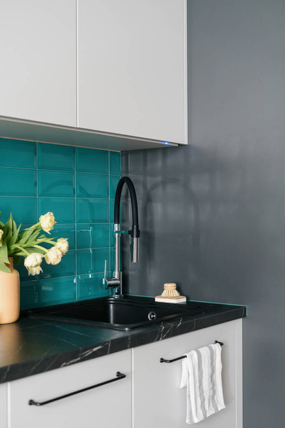detalle en la cocina con interior moderno, fregadero negro, grifo de cromo contemporáneo, encimera de mármol, armarios de muebles blancos y azulejos azules en la pared - Foto, Imagen