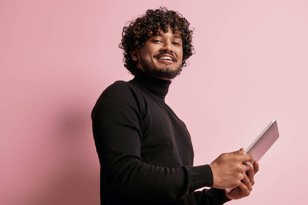 Handsome Indian man holding digital tablet and smiling against pink background - Foto, imagen