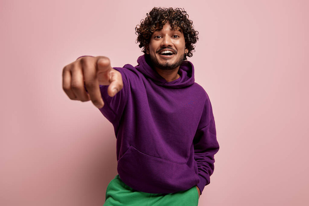 Handsome Indian man pointing camera and smiling against pink background - Zdjęcie, obraz