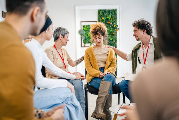 Un grupo de personas sentadas en un círculo con dos terapeutas y una mujer en el centro discutiendo y brindando apoyo emocional para ella. - Foto, Imagen