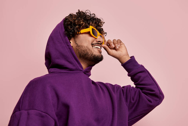 Happy young Indian man adjusting his sunglasses against pink background - Foto, imagen