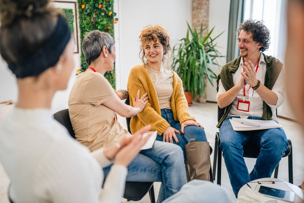 Skupina lidí sedících v kruhu se dvěma terapeuty a ženou v centru, diskutující a poskytující jí emocionální podporu, se zaměřuje na ženu, ale všichni se věnují konverzaci. - Fotografie, Obrázek