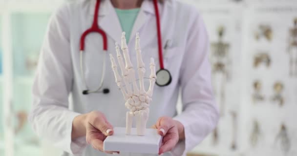 Ärztin mit Stethoskop hält Handskelett. Mediziner präsentiert Studenten Skelett eines Armteils nähere Zeitlupe - Filmmaterial, Video