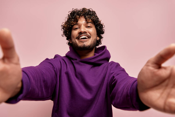Low angle view of happy young Indian man stretching out hands against pink background - Valokuva, kuva