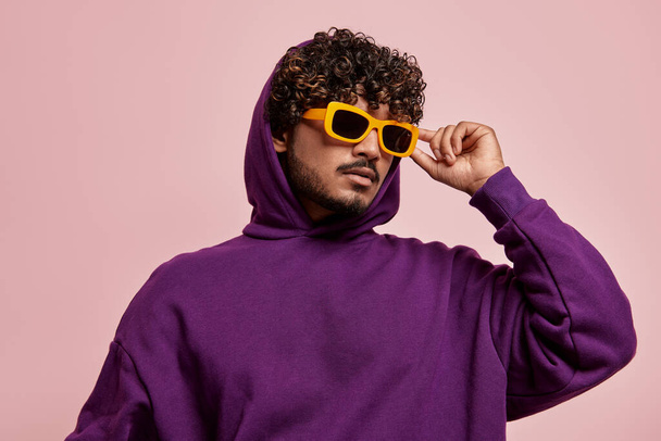 Handsome young Indian man adjusting his sunglasses against pink background - Фото, зображення