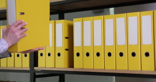 Woman employee putting back yellow ring binder with accounting papers to office archive. Organized folders structure with materials on shelf of rack - Footage, Video