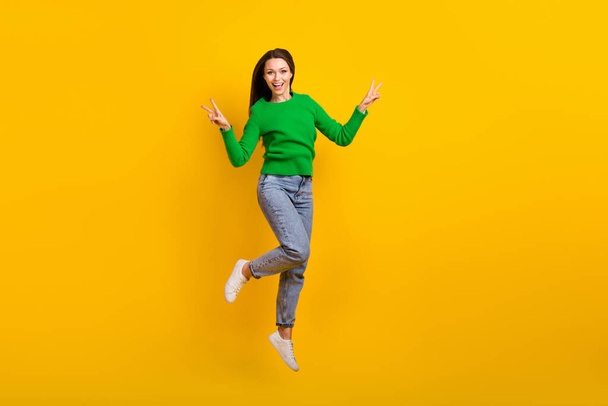 Full size photo of overjoyed energetic girl jumping demonstrate v-sign isolated on yellow color background. - Fotó, kép