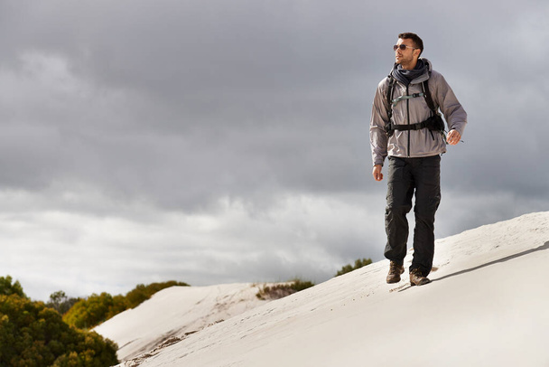 He handles these hills like a seasoned hiker. a young male hiker walking along the sand dunes - Фото, изображение