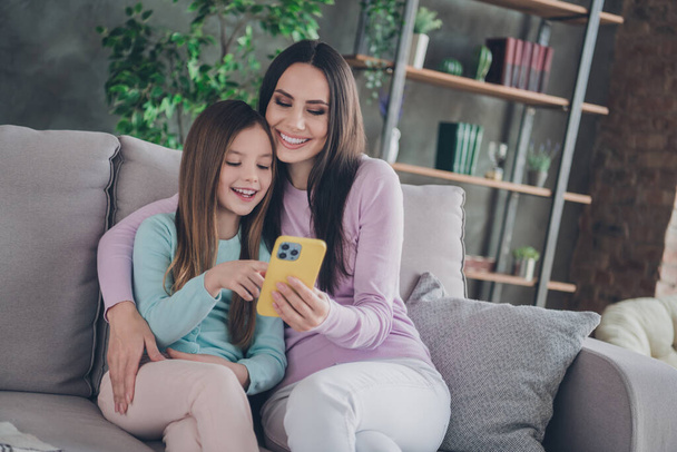 Photo of caring mom mommy hug her little kid girl sit comfort couch use gadget reading news feed in social network. - Фото, изображение