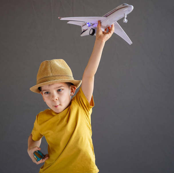 A child in summer clothes and sunglasses sits on a suitcase and holds a toy airplane in his hands. Waiting for travel. Family vacation. Dreams of travel. Summer vacation - Photo, image