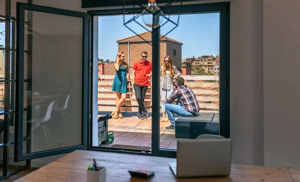 Veduta del lavoro di squadra che parla sul tetto della città attraverso una porta di vetro dell'ufficio di coworking in una giornata di sole - Foto, immagini