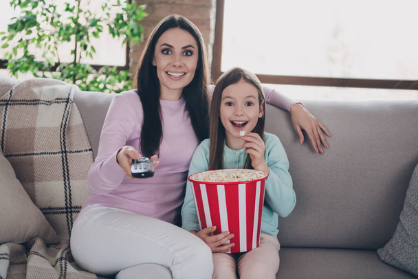 Photo of cute excited daughter mom dressed casual clothes eating pop corn watching tv indoors apartment room. - Fotó, kép