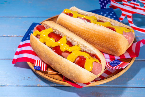USA Patriotic picnic holiday hot dogs.  American patriotic hot dog on wooden board plate, with USA flag. Celebrating Independence day on 4th July, Memorial or Veteran Day - 写真・画像