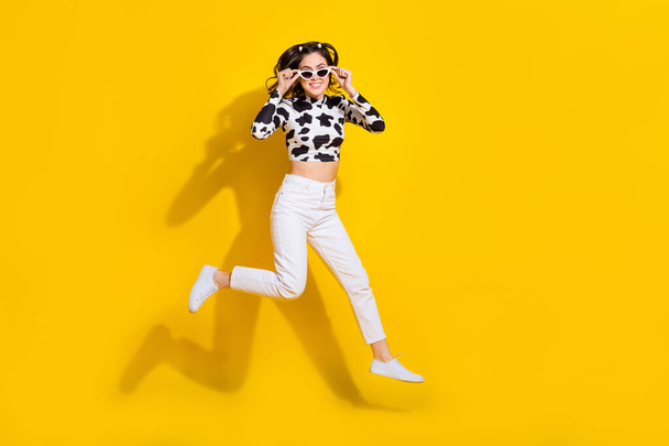 Full length photo of funny cool lady dressed cowskin shirt arms dark eyewear jumping high empty space isolated yellow color background. - Foto, Imagem